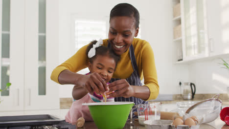 Happy-african-american-mother-and-daughter-wearing-aprons-cooking-in-kitchen