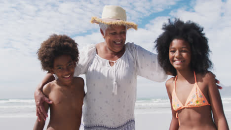 Portrait-of-mixed-race-senior-woman-with-grandchildren-smiling-at-the-beach