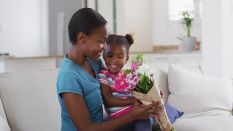 Feliz-Madre-E-Hija-Afroamericana-Sentadas-En-El-Sofá-Y-Oliendo-Flores