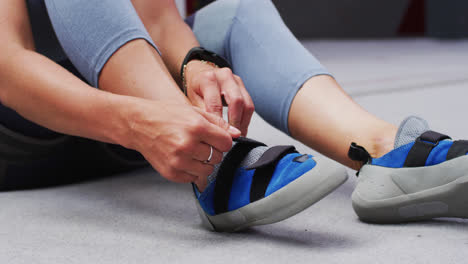 Low-section-of-caucasian-woman-putting-on-climbing-shoes-at-indoor-climbing-wall