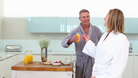 Mature-smiling-man-bringing-his-wife-a-glass-of-orange-juice-at-breakfast