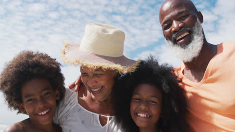 Portrait-of-mixed-race-senior-couple-with-grandchildren-smiling-at-the-beach