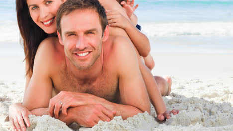 Portrait-of-smiling-caucasian-family-on-holiday-lying-on-sand-by-sea