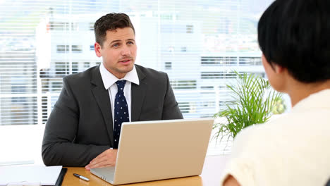 Businessman-with-laptop-interviewing-a-woman-at-his-desk