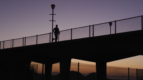 Silhouette-of-man-running-on-bridge-in-the-evening
