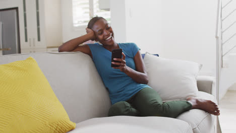 Glückliche-Afroamerikanische-Mutter-Sitzt-Mit-Smartphone-Auf-Dem-Sofa-Und-Lacht