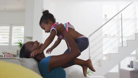 Happy-african-american-mother-and-daughter-sitting-on-sofa-and-hugging