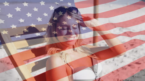 Animation-of-american-flag-waving-over-smiling-woman-in-deckchair-on-beach