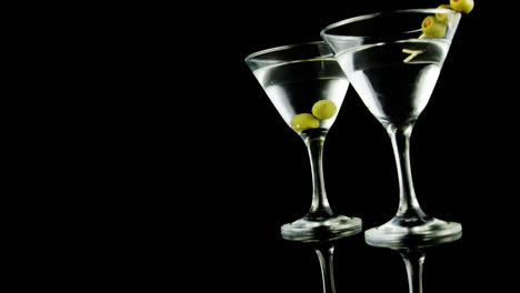 Chevron-Muster-Design-über-Oliven-In-Zwei-Cocktailgläsern-Vor-Schwarzem-Hintergrund