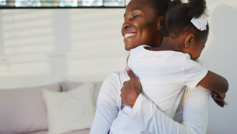 Happy-african-american-mother-and-daughter-sitting-on-bed-and-hugging