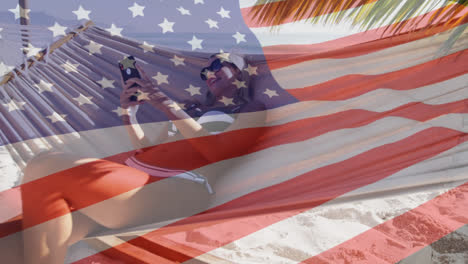 Animation-Einer-Amerikanischen-Flagge,-Die-über-Einer-Frau-In-Einer-Hängematte-Weht-Und-Ihr-Smartphone-Am-Strand-Benutzt