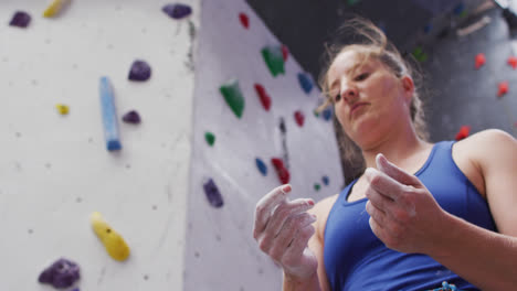 Caucasian-woman-preparing-her-hands-with-chalk-before-climbing-at-indoor-climbing-wall