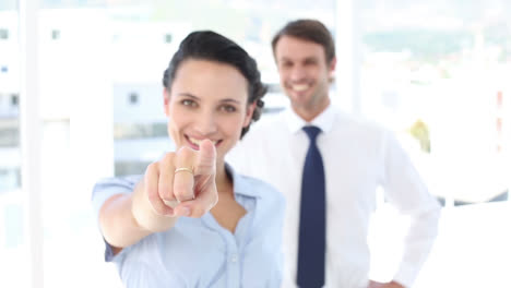 Businesswoman-pointing-at-camera-with-colleague-behind-her