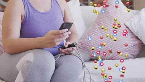 Animation-of-emojis,-like-and-love-icons-over-woman-using-smartphone,-during-exercise-at-home