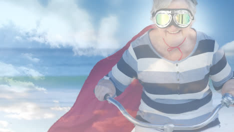 Animation-of-glowing-light-over-happy-senior-woman-superhero-on-bike-by-seaside