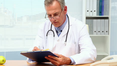Doctor-writing-on-clipboard-at-his-desk