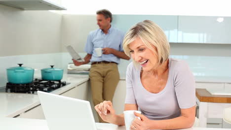 Woman-using-laptop-while-her-husband-is-standing-reading-the-newspaper