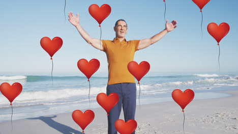 Animation-of-red-heart-love-balloons-digital-icons-over-smiling-senior-man-on-beach