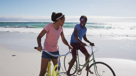 Afroamerikanisches-Paar-Lächelt-Und-Fährt-Fahrrad-Am-Strand