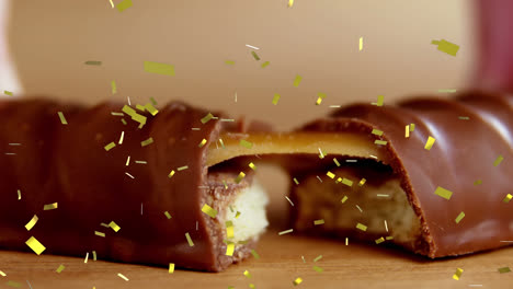 Animation-of-gold-confetti-falling-over-broken-biscuit-and-caramel-chocolate-bar
