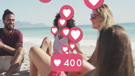 Animation-of-love-heart-digital-icons-and-numbers-over-group-of-friends-on-beach