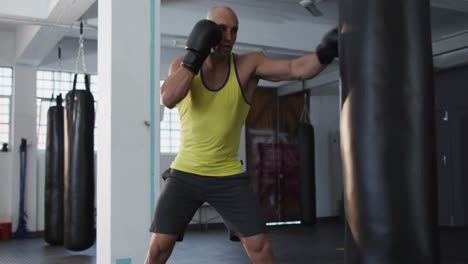 Caucasian-male-trainer-wearing-boxing-gloves-training-with-punching-bag-at-the-gym