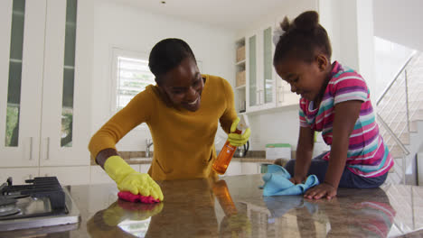 African-american-mother-and-daughter-cleaning-countertops-and-laughing-in-kitchen