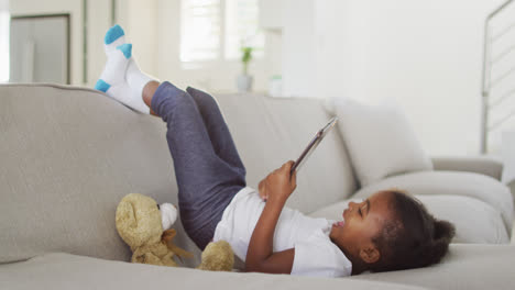 African-american-happy-girl-lying-on-sofa-using-digital-tablet-at-home