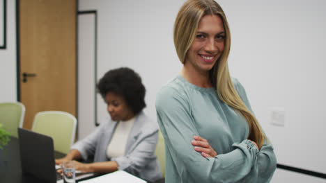 Portrait-of-caucasian-businesswoman-smiling-in-office,-with-colleague-working-in-background