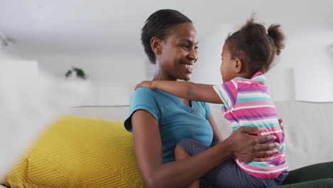 Happy-african-american-mother-and-daughter-sitting-on-sofa-and-touching-foreheads