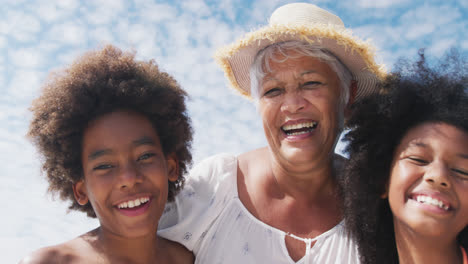 Portrait-of-mixed-race-senior-woman-with-grandchildren-smiling-at-the-beach