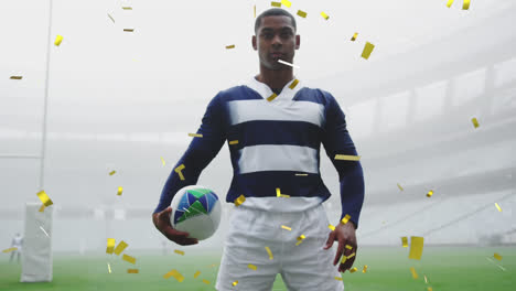 Confetti-falling-over-african-american-male-rugby-player-holding-a-ball-against-sports-stadium