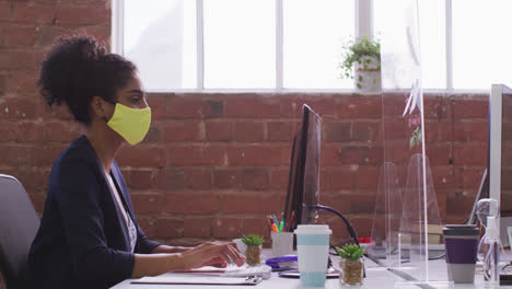 Mixed-race-businesswoman-typing-sitting-in-front-of-computer-wearing-face-mask