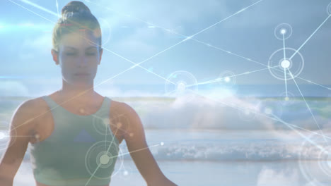 Animation-of-network-of-connections-over-woman-practicing-yoga-by-the-beach