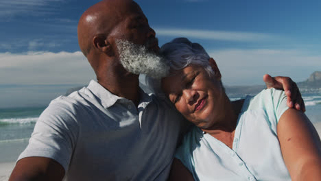 Glückliches-älteres-Afroamerikanisches-Paar,-Das-Am-Strand-Sitzt-Und-Umarmt