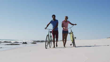 Afroamerikanisches-Paar-Spaziert-Mit-Fahrrädern-Am-Strand