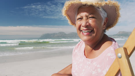 Portrait-of-mixe-race-senior-woman-sitting-on-subed-and-smiling-at-the-beach