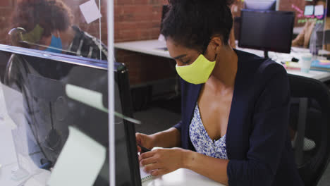 Mixed-race-businesswoman-having-video-chat-sitting-in-front-of-computer-wearing-face-mask