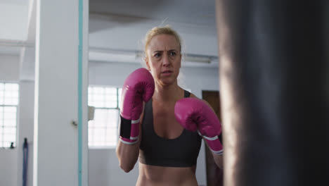 Caucasian-female-boxer-wearing-boxing-gloves-kicking-the-punching-bag-at-the-gym