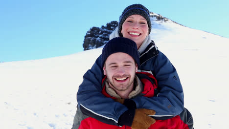 Smiling-man-giving-his-girlfriend-a-piggy-back-in-the-snow
