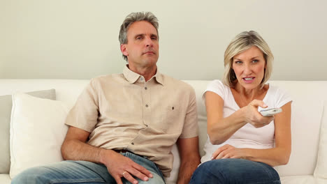 Woman-stealing-the-remote-control-from-her-dozing-husband-on-the-couch