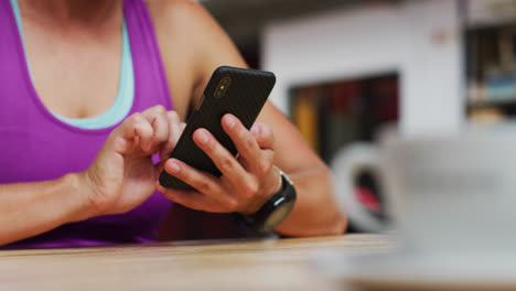 Midsection-of-caucasian-woman-using-smartphone-sitting-at-cafe-in-gym