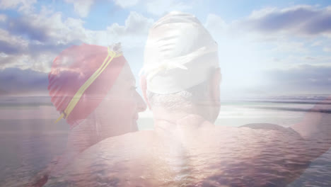 Animation-of-glowing-light-over-happy-senior-couple-in-swimming-hats-by-seaside