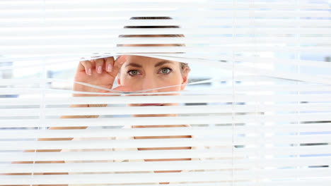 Frowning-businesswoman-peeking-through-the-blinds