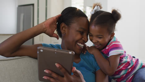 Glückliche-Afroamerikanische-Mutter-Und-Tochter-Sitzen-Auf-Dem-Sofa-Mit-Digitalem-Tablet-Und-Lachen