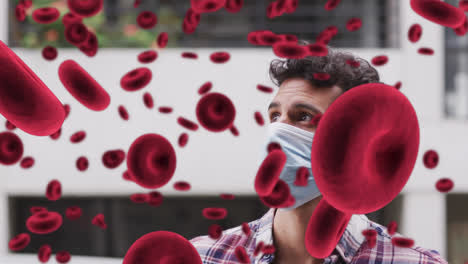 Animation-of-floating-red-blood-cells-over-man-wearing-face-mask-in-city-street