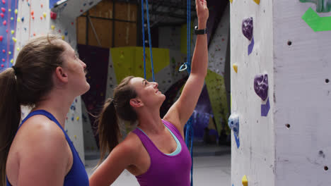 Two-happy-caucasian-women-talking-and-preparing-for-a-climb-at-indoor-climbing-wall