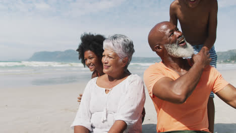 Portrait-of-mixed-race-senior-couple-with-grandchildren-playing-and-smiling-smiling-at-the-beach