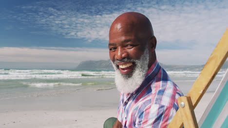 Portrait-of-mixe-race-senior-man-sitting-on-subed-and-smiling-at-the-beach