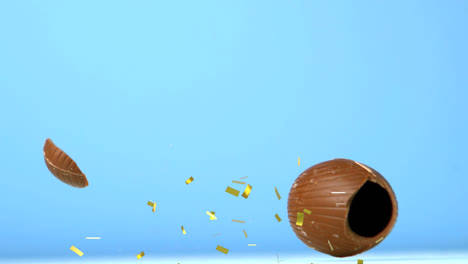 Animation-of-gold-confetti-falling-over-chocolate-easter-egg-falling-and-breaking,-on-blue